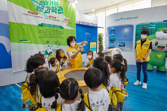 경남 거제시에 마련된 2021년 찾아가는 작은 과학관)에서 어린이들이 전시물 시연 설명을 듣고 있다.