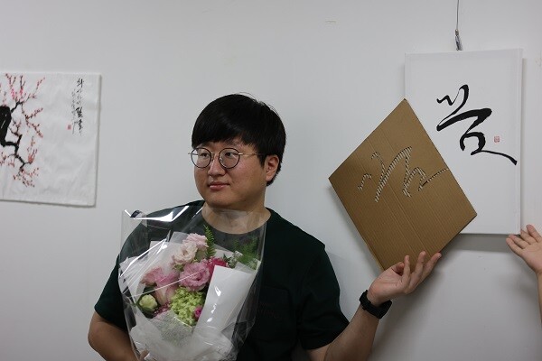 '''당신의 꿈, 응원합니다' 황도원 작가가 지인에게 건네받은 꽃선물을 들고 기념 촬영을 하고 있다. 지난 18일 오후 대구 범어지하도상가 6, 7번 출구 일대 황도원 작가 캘리그라피 작품 전시회가 열린 현장. 사진=남경원 기자