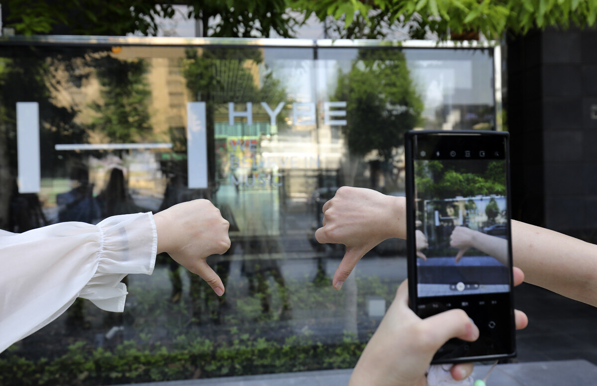 해외 아미들이 하이브 사옥 앞에서 하이브에 항의하는 손동작을 하며 인증샷을 담고 있다.