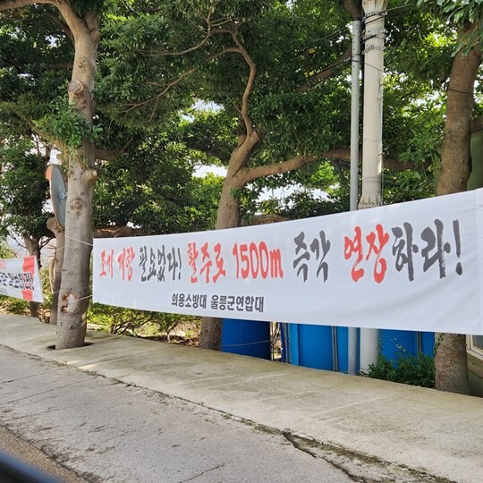 울릉공항 공사 현장 인근 있는 공사 노동자 숙소 입구에 내걸린 의용소방대 울릉군연합대 현수막. '조기 개항 필요없다! 활주로 1500m 즉각 연장하라!' 문구가 적혀 있다. 사진=김지영 기자